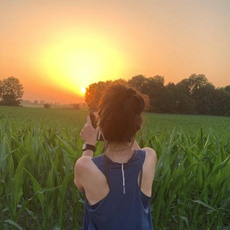 Henriette steht am Rand eines Weizenfeldes und blickt in den warmen Sonnenuntergang